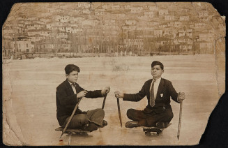 Portrait photographique noir et blanc sous forme de carte postale de deux jeunes hommes  assis en tailleur sur une espèce de luge en bois